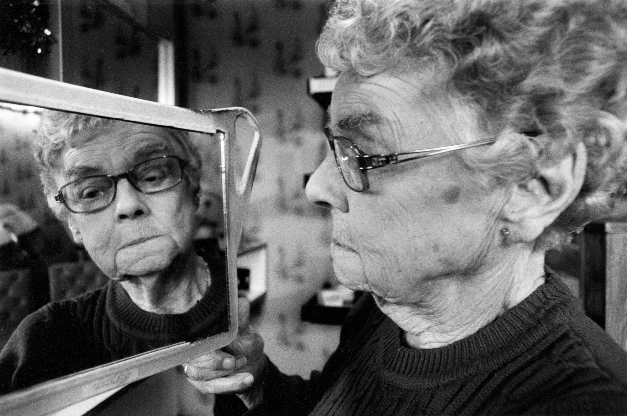 Elderly woman looks at her hair in mirror held to face